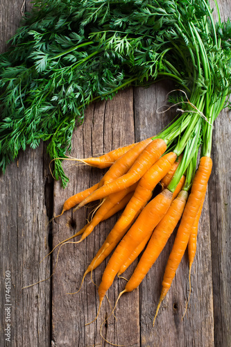 Raw carrot with green leaves on wooden background