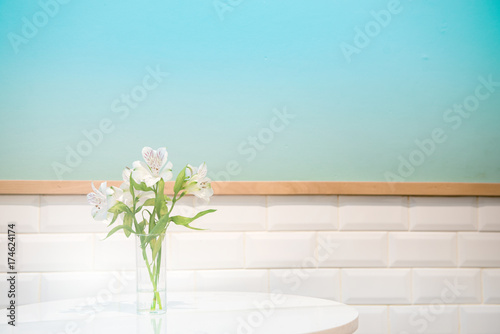 Beautiful white flower in glass vase on turquoise background and white crick tiles wall. Festive greeting card