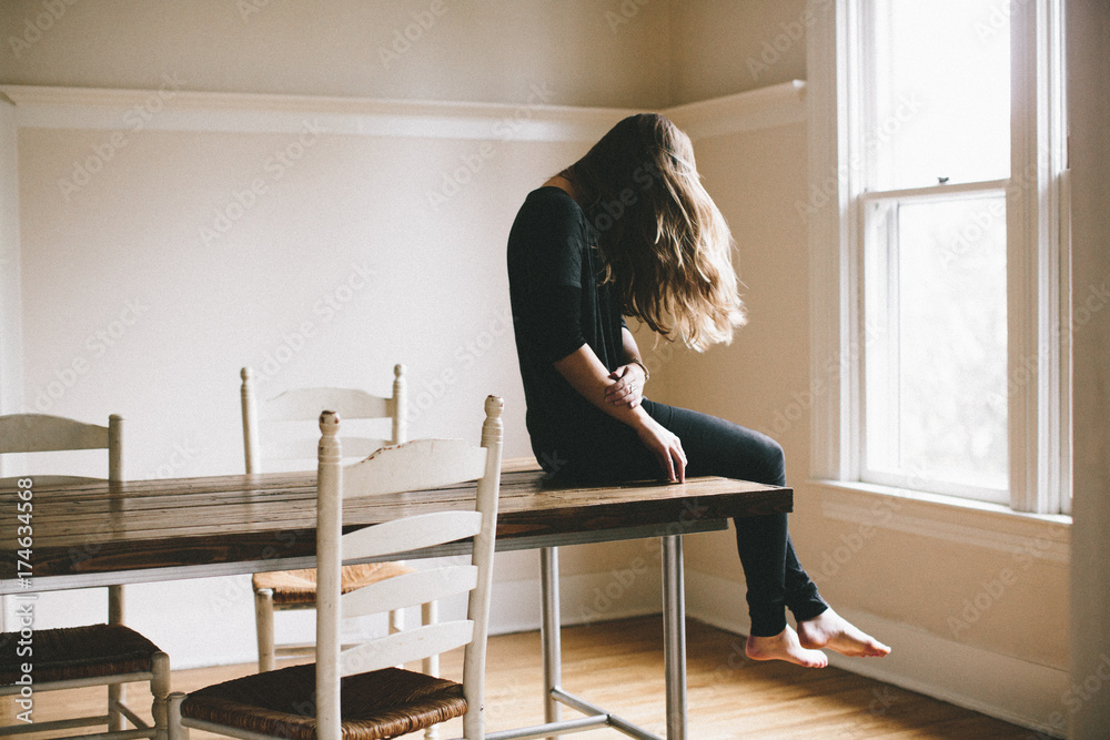 young woman sitting on a table facing window young woman sitting on a table facing window