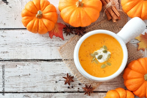 Autumn pumpkin soup, rustic overhead scene on a white wood background