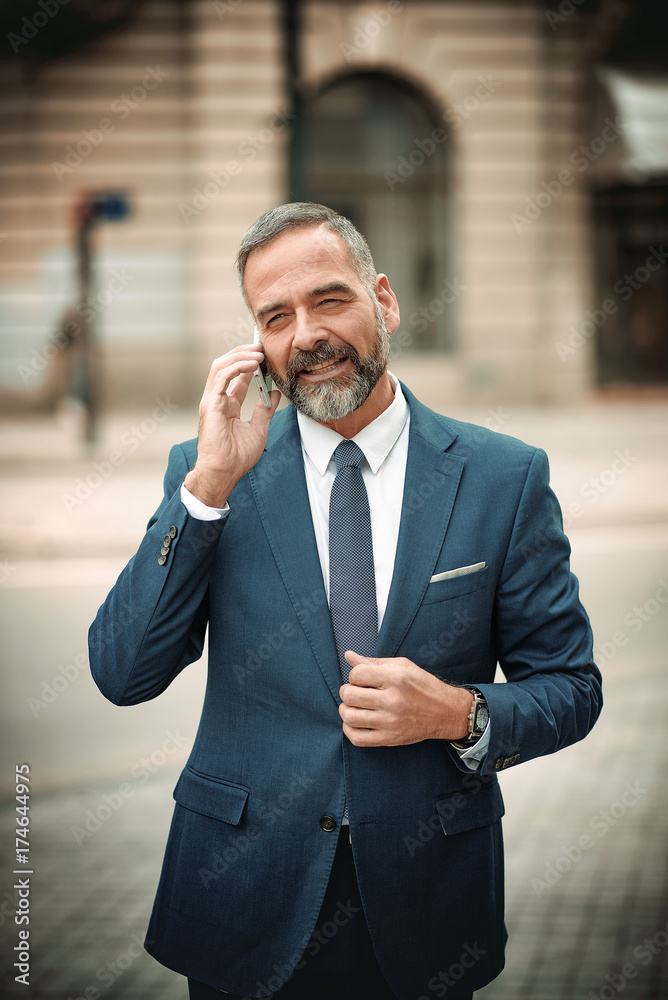 Smart senior business man, an elderly entrepreneur and business owner, talking over his cell phone in an outdoors urban area Smart senior business man, an elderly entrepreneur and business owner, talking over his cell phone in an outdoors urban area
