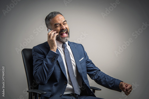 Senior aged business owner yelling at his cell phone, sitting in his office chair