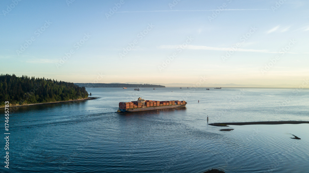 Big Cargo Ship fully loaded is leaving port and passing by Stanley Park, Vancouver, British Columbia, Canada.