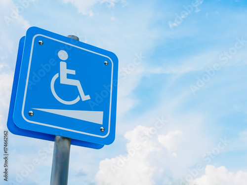 Wheelchair symbol in a parking lot with blue and white sky background.