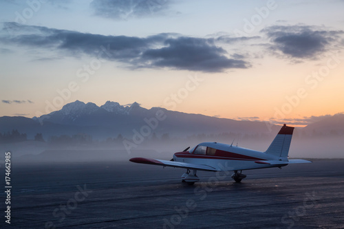 Airplane parked at the airport during a colorful and vibrant sunrise with mouhtains in the background. Taken in Pitt Meadows, Greater Vancouver, BC, Canada.