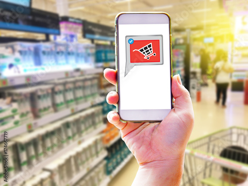 Woman hand holding smartphone and shopping at the supermarket - Learning app for shopping cart and connecting with her smartphone with online shopping of concept