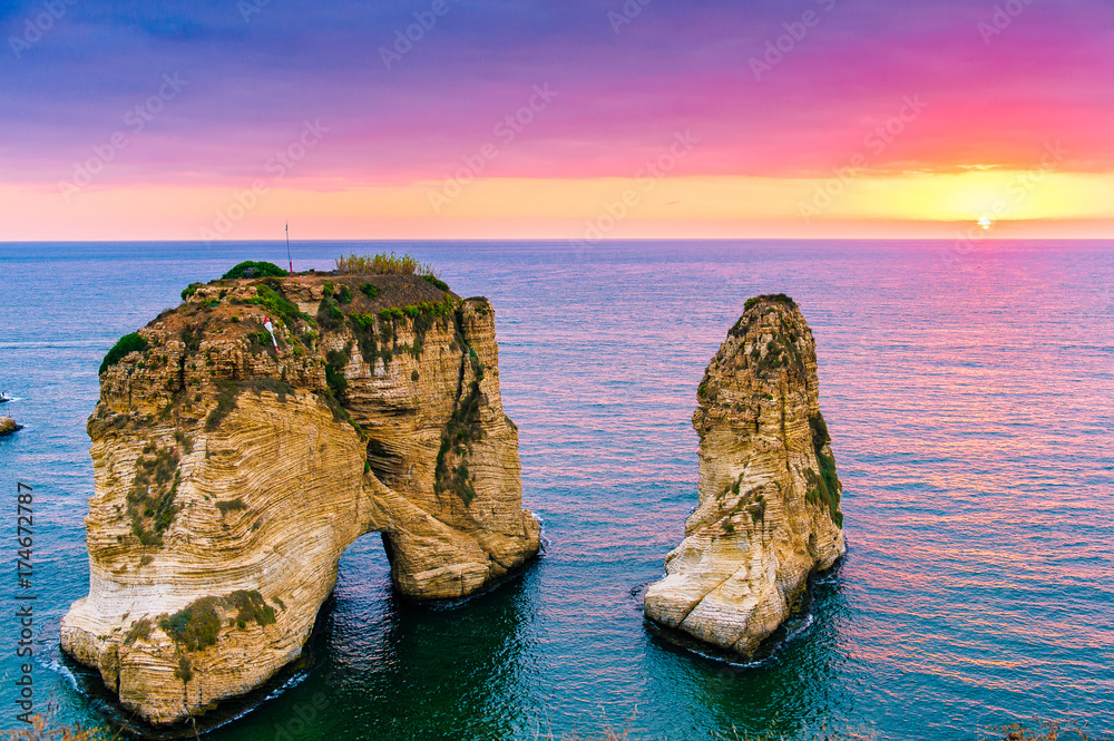 Fototapeta premium Piękny zachód słońca na Raouche, Pigeons 'Rock. W Bejrucie w Libanie Słońce i kamienie odbijają się w wodzie, gęste chmury na niebie.