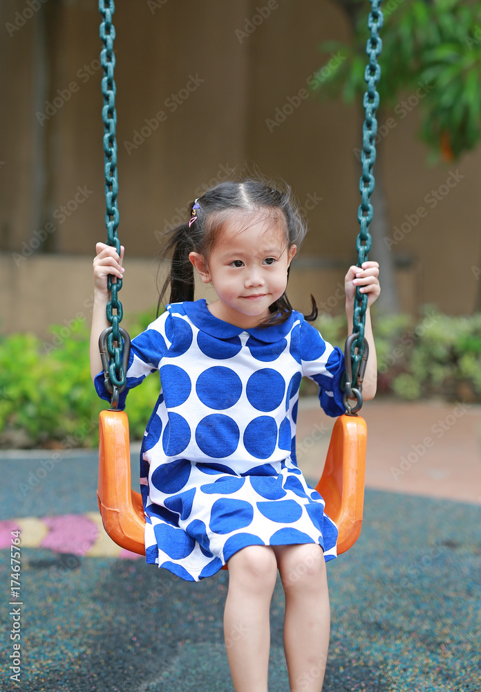 Adorable kids girl playing at the swing in the playground.