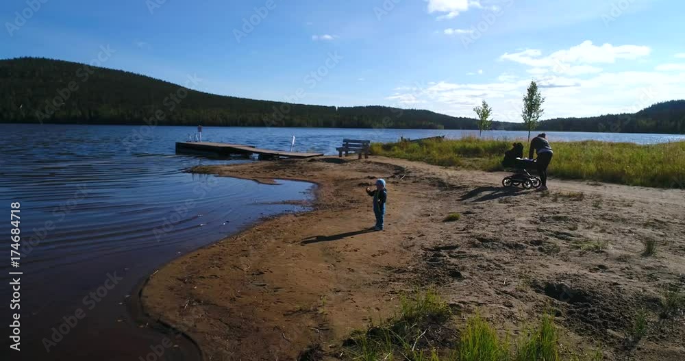 Family on a beach,, aerial view around kid playing at the water, infront of a mother and a baby carry on a sandy coast, at lake pyhajarvi, in the arctic taiga wilderness of Lapland, in Lappi, Finland Family on a beach,, aerial view around kid playing at the water, infront of a mother and a baby carry on a sandy coast, at lake pyhajarvi, in the arctic taiga wilderness of Lapland, in Lappi, Finland