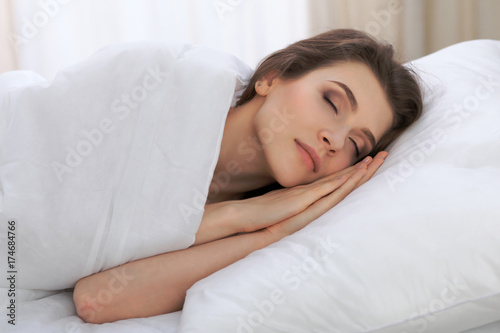 Beautiful young woman sleeping while lying in her bed and relaxing comfortably. It is easy to wake up for work or the day off. Concept of pleasant and rest reinstatement for active life