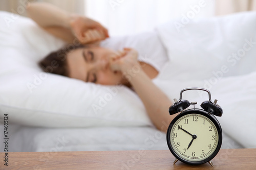 Beautiful sleeping woman resting in bed and trying to wake up with alarm clock