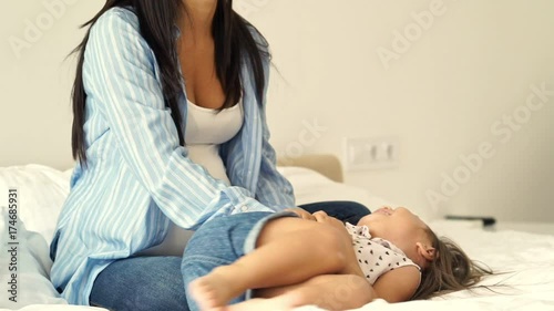 Happy asian mother tickles her daughter on bed at home photo