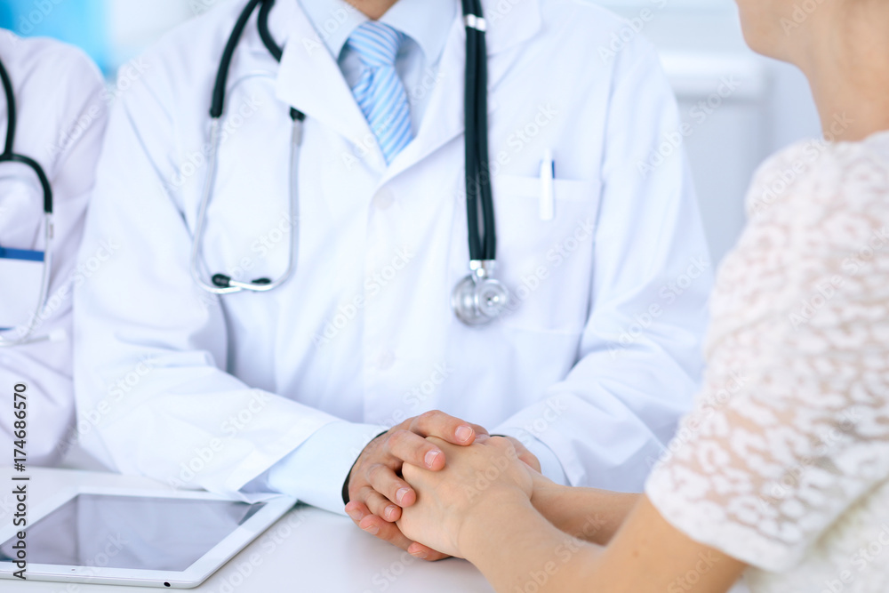 Doctor reassuring his female patient by touching her hands while talking. Symbol of support and trust in medicine