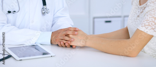 Doctor reassuring his female patient by touching her hands while talking. Symbol of support and trust in medicine