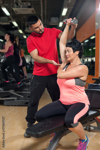 Middle aged woman working out with coach in gym