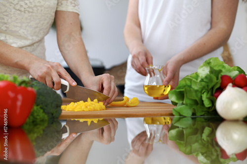 Close-up of human hands cooking in a kitchen. Friends having fun while preparing fresh salad. Vegetarian, healthy meal and friendship concept
