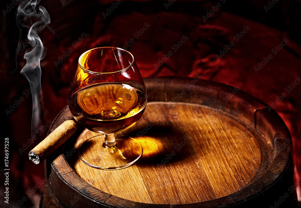 Cognac and Cigar on old oak barrel.Red stone background