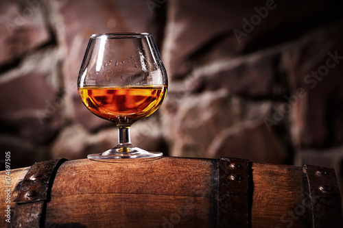 Fotografia Glass of cognac on the old wooden barrel