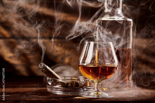 Glass of cognac or brandy with smoking cigar on wooden table.A lot of smoke photo