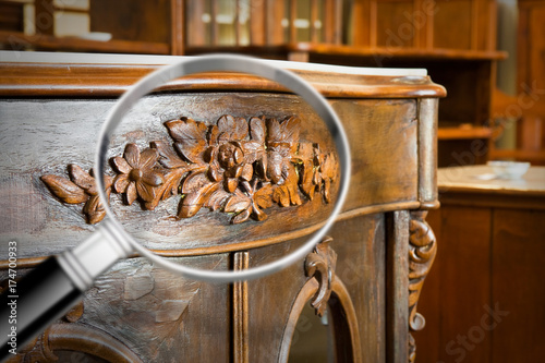 Detail of an antique wooden italian furniture just restored with a magnifying glass on foreground looking for woodworm threat detection