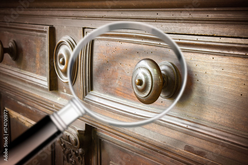 Detail of an antique wooden italian furniture just restored with a magnifying glass on foreground looking for woodworm threat detection