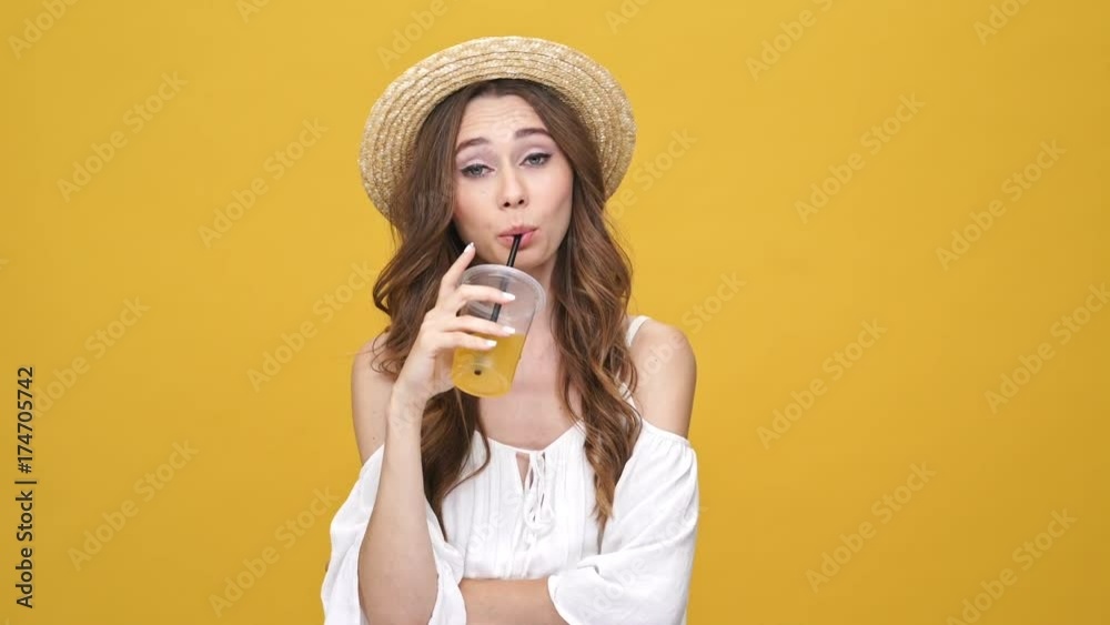 Displeased brunette woman in dress and hat drinking juice and shrugs her shoulders over orange background
Displeased brunette woman in dress and hat drinking juice and shrugs her shoulders over orange background