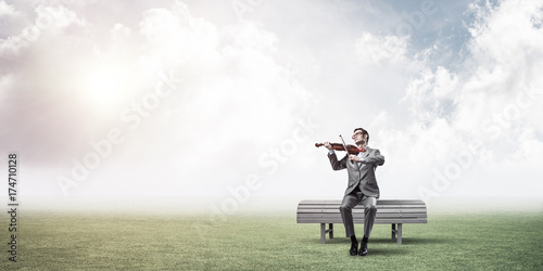 Handsome businessman in park on wooden bench play his melody