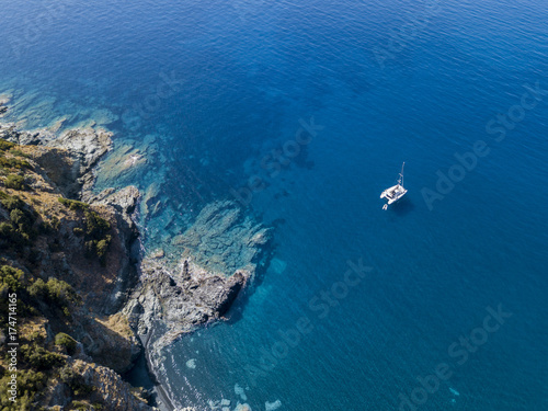 Vista aerea di una scogliera a picco sul mare e di un catamarano ormeggiato, barca. Penisola di Cap Corse, Corsica. Tratto di costa. Francia