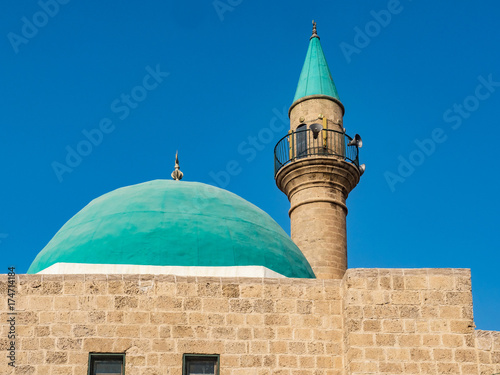 Stone mosque with a minaret with domes of green color against the blue sky