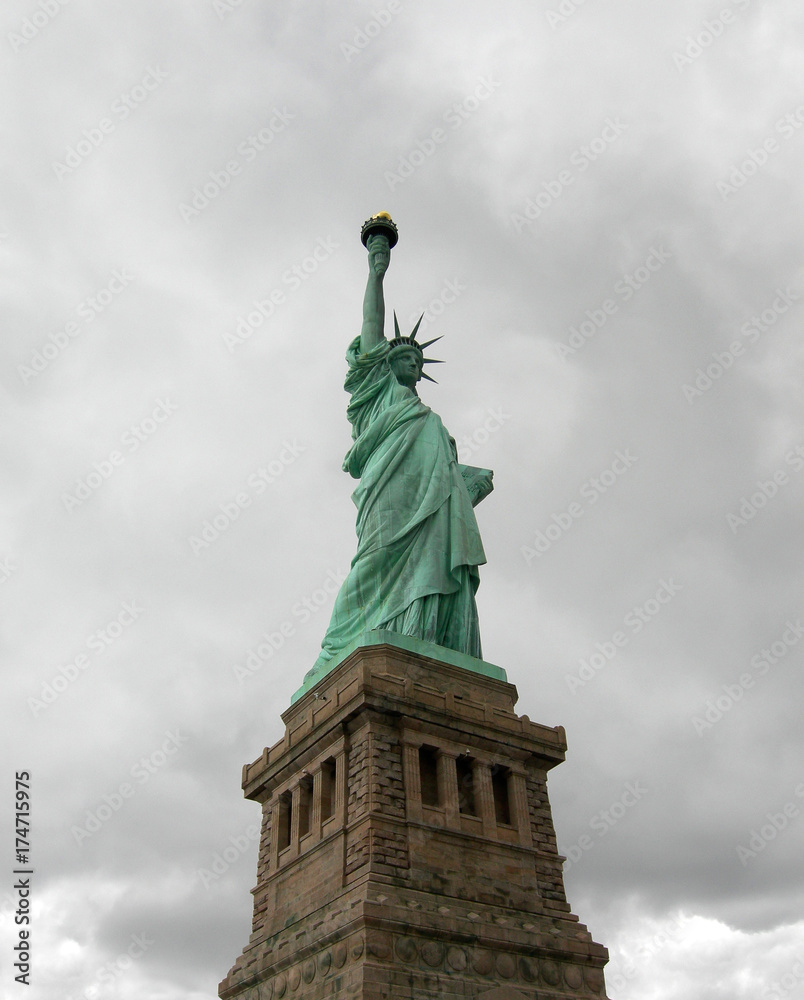 Fototapeta premium Statue of liberty seen from the front with a grey and cloudy sky as background in Manhattan, New York City.