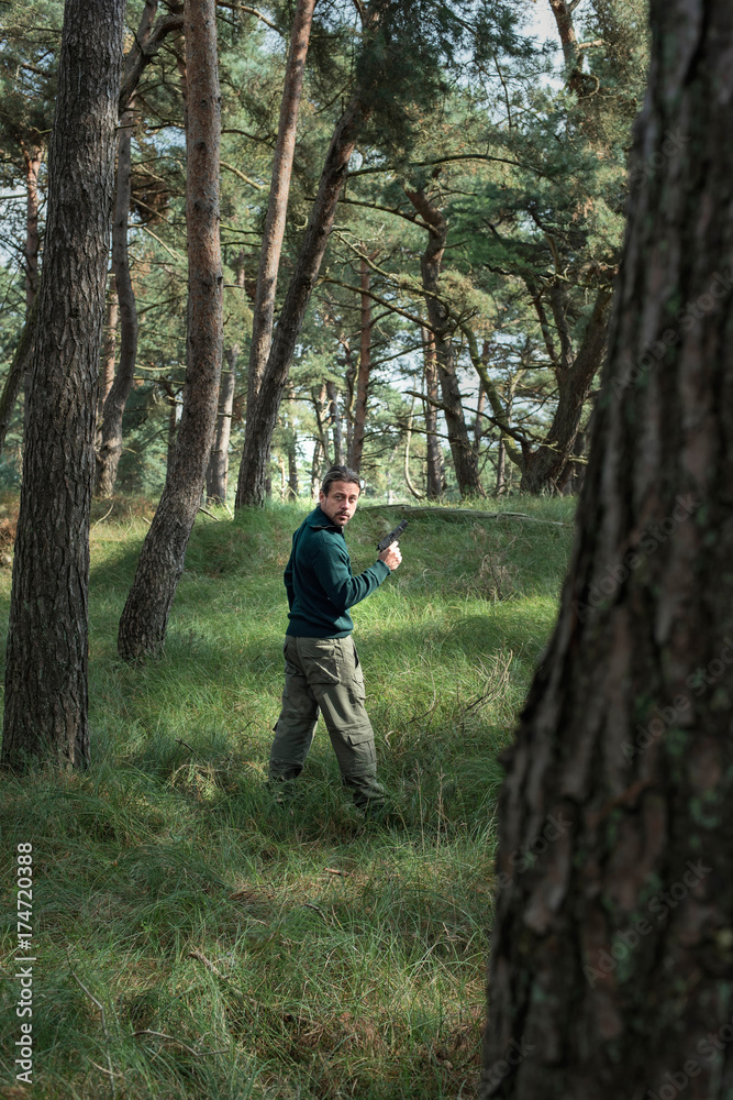 Man with pistol standing in pine forest. Side view. Man with pistol standing in pine forest. Side view.