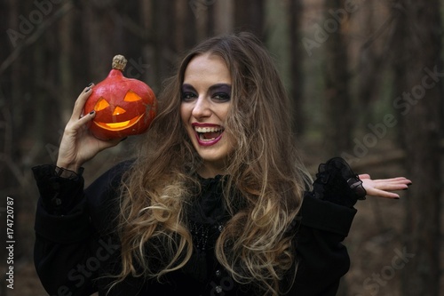 Halloween. beautiful girl with a pumpkin in a black dress in the forest.
