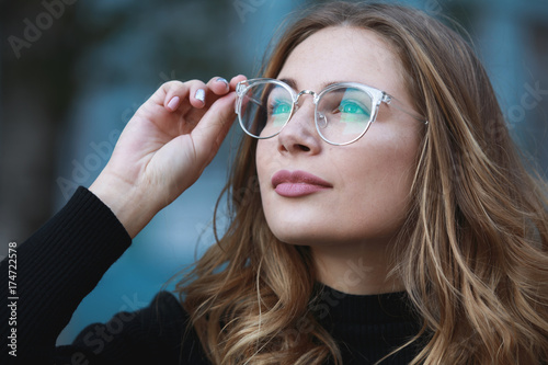 Myopia, close-up portrait of young woman student in eyeglasses for good vision looking up, blue building background