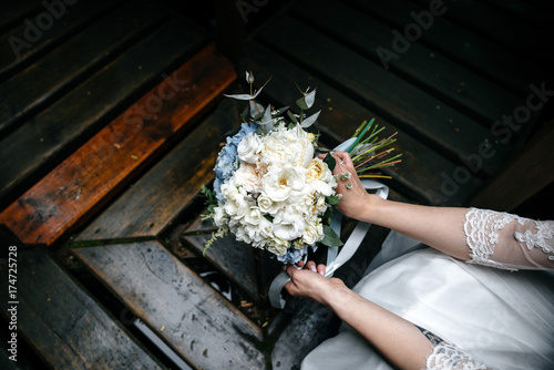 Wedding bouquet of white flowers in the gentle hands of the bride. Concept wedding, love, marriage, creation of seven, wedding details. bouquet on a dark background. photo