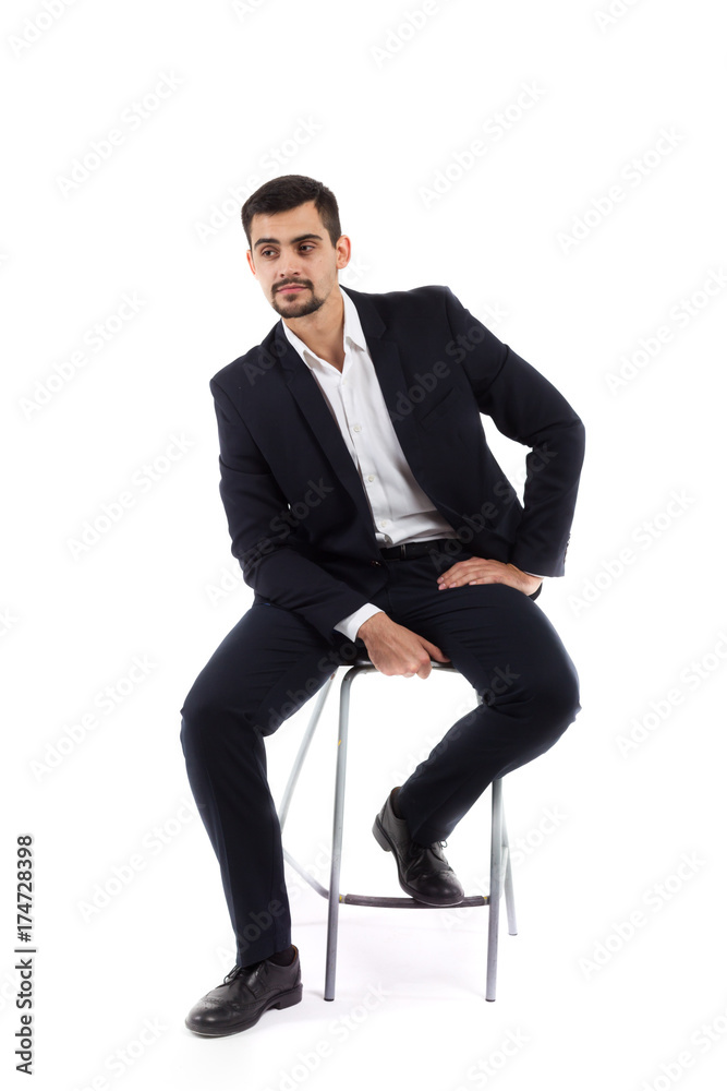 A young man sits on a bar high chair, a business suit, a serious look, is inexhaustible or a financier, or an office employee. Isolate on white background. A young man sits on a bar high chair, a business suit, a serious look, is inexhaustible or a financier, or an office employee. Isolate on white background.