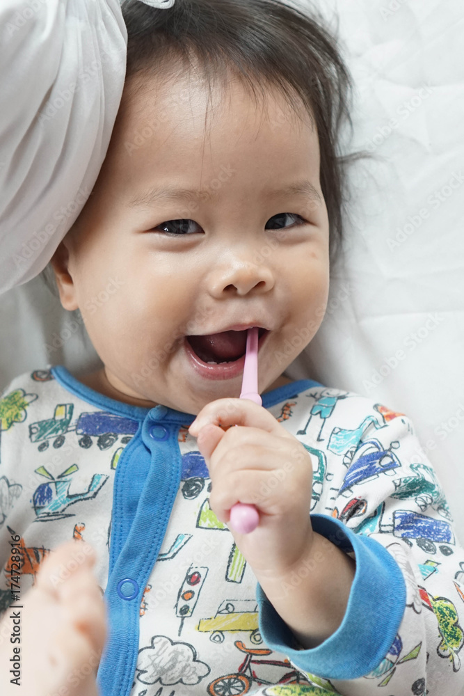 Happy of little toddler baby girl brushing her teeths by herself. Smiling with brush teeth lay on white sheet bed Happy of little toddler baby girl brushing her teeths by herself. Smiling with brush teeth lay on white sheet bed