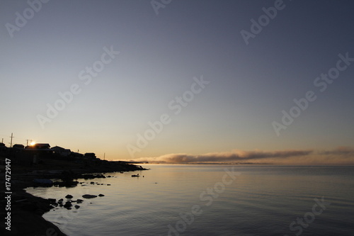 Beautiful sunrise over an arctic lake with fog on the horizon and sun peaking over buildings