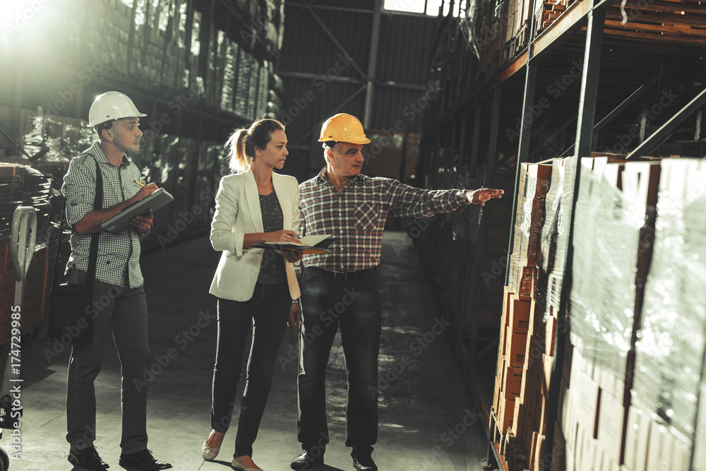 Team of customs managers and warehouse worker checking list and inventory on the shelf in storehouse.