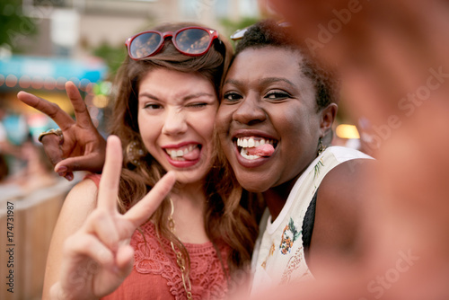 Diverse group of two girls taking selfies photos in the crowd of a summer music festival