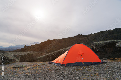 An orange high-altitude tent is set high in the mountains against the background of the Caucasian ridge