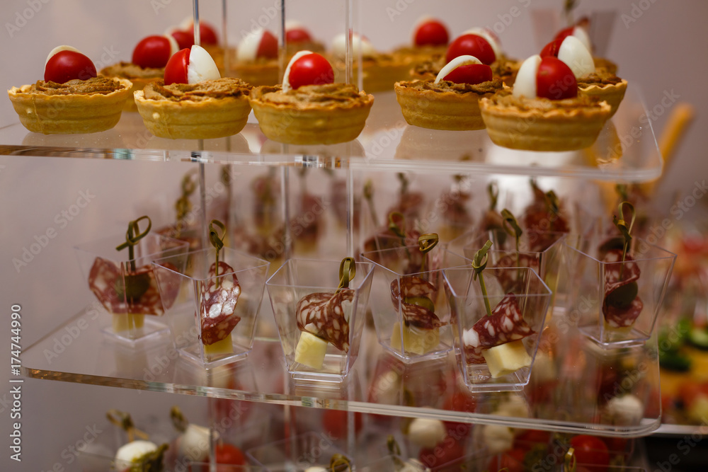 Catering for party. Close up of appetizers with cherry tomatoes, green olives, olive oil, cheese and spices in short glasses on wood brown table.