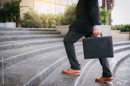 Businessman walking up the stairs and holding a briefcase in hand working with confidence photo