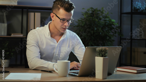 Portrait of tired business man in casual shirt working in the laptop in the stylish office, feeling very exausted. photo