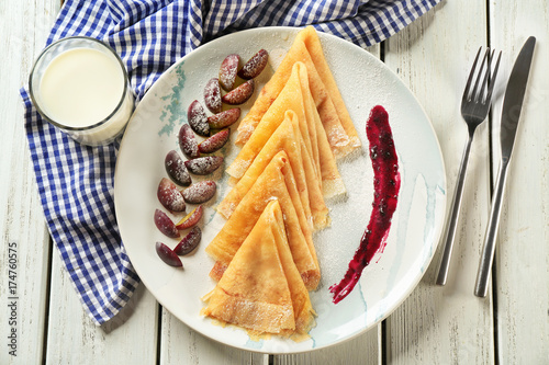 Plate with tasty thin pancakes and plums on table