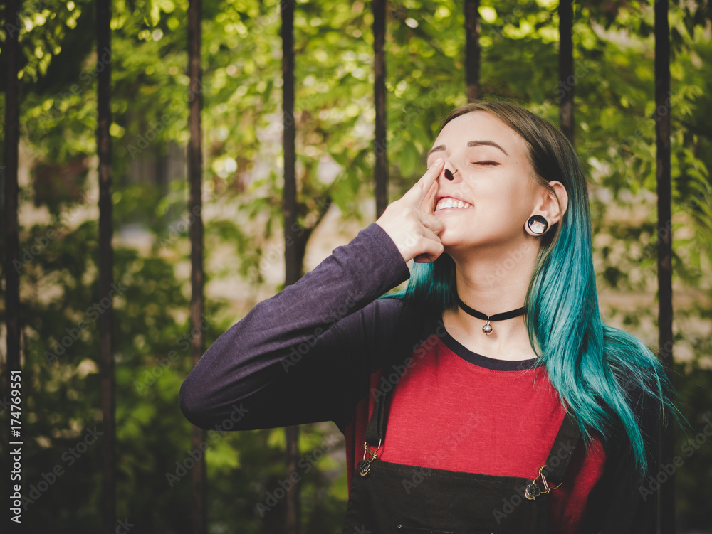 Street punk or hipster girl enjoying empty old European street. Portrait of teen girl with blue dyed hair,piercing in nose,violet lenses and unusual hairstyle.