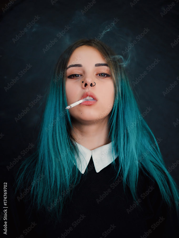 Emo girl smoking cigarette. Young student or pupil with blue colorful dyed  hair, hat, piercing,lenses,ears tunnels and unusual hairstyle stands on  black background. Stock Photo | Adobe Stock