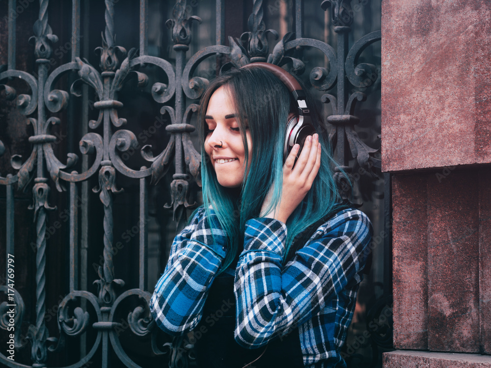 Street hipster girl listening music with brown headphones. Teen girl with  blue dyed hair,piercing in nose,violet lenses,unusual hairstyle sitting  near historic building. Stock-Foto | Adobe Stock
