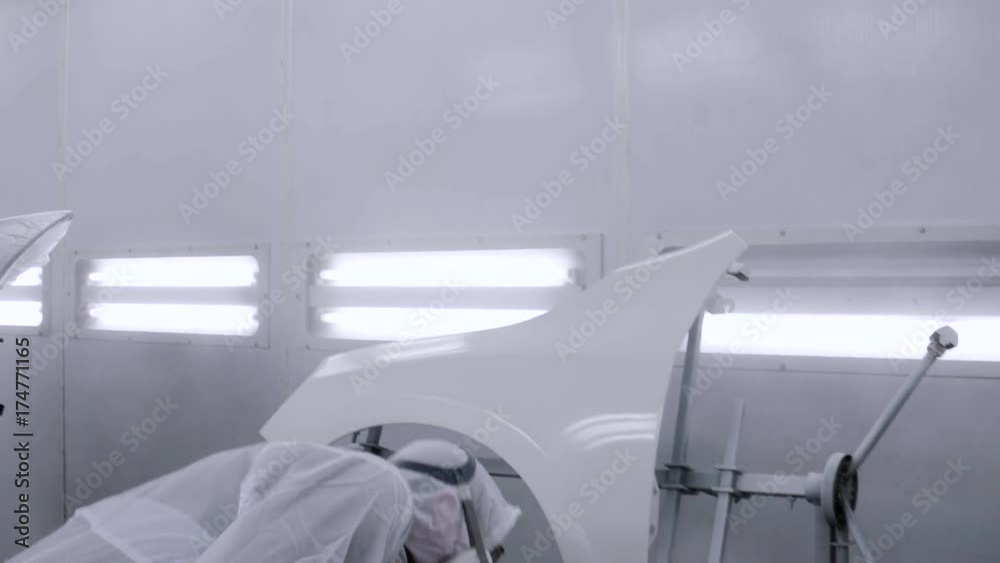 A professional car painter is painting the body work of a car in a paint box of a garage with an airbrush.