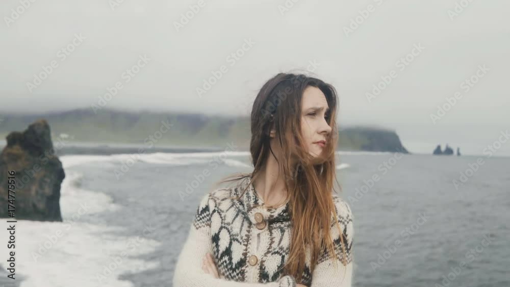 Young beautiful woman standing on the black beach, near the Troll toes in Iceland and looking around in windy day. Young beautiful woman standing on the black beach, near the Troll toes in Iceland and looking around in windy day.