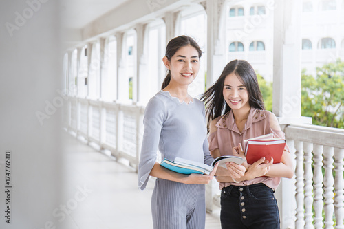Фотография Asian student sitting outside school building reading book, Two asian girls reading book together